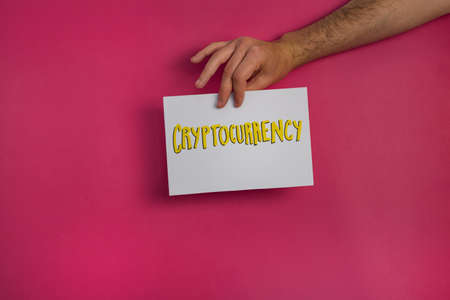 A closeup shot of a man holding a paper with the word "CRYPTOCURRENCY" on a fuchsia backgroundの写真素材