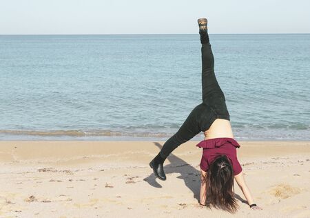 woman has fun at the beach doing gymnastic exercises - a girl enjoys the day - desaturated pastel...