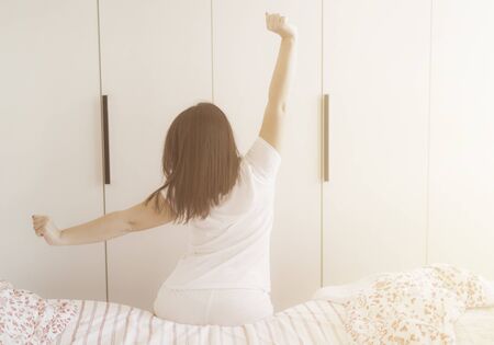 Beautiful woman waking up in her bed, she is stretching her shoulders and armsの写真素材