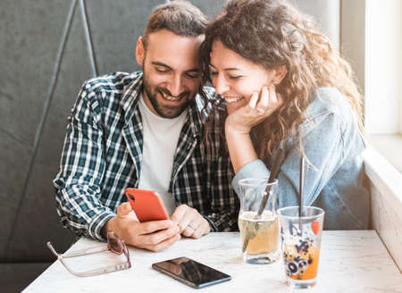 Engaged couple enjoying time together using smartphone - Friends are having fun in a bar with mobile...