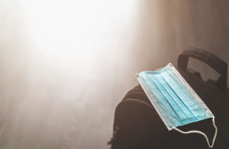 Close up of a backpack with surgical mask - travel concept with individual protections during the coronovarius pandemic - focus on the mask with flare on the backgroundの写真素材