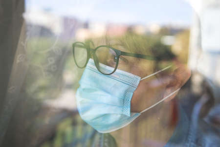Portrait of a middle-aged woman looking out the window - Woman worried in quarantine during the...