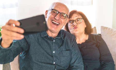 Portrait of joyful senior married couple - Retired couple enjoying free time taking funny selfie - middle-aged couple having fun together using smartphoneの写真素材