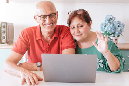 Middle aged couple chatting in video call with their friends and relatives during the lockdown - Happy mature couple keeps social distances using videochat - quarantined videocall conceptの写真素材