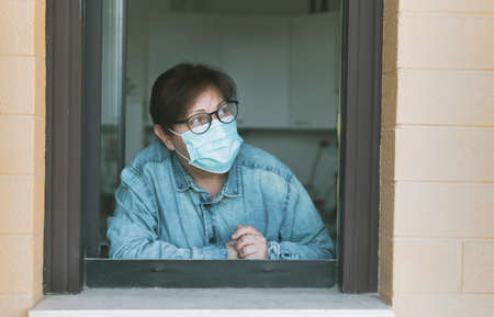 Portrait of a worried woman looking out to balcony - thoughtful middle aged woman looks out window -...