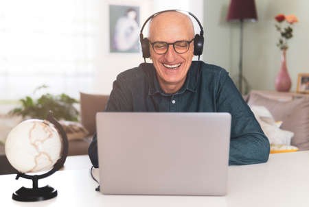 Man listening to music on headphones while working on the computer from home - Middle aged man having fun in conference - warm contrast filterの写真素材