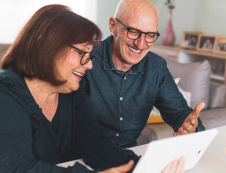 Senior middle aged happy couple embracing using tablet together - smiling elderly family reading the news and shopping online from home - mature people and technology conceptの写真素材