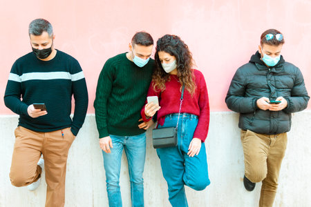 Young people keep social distance, using smart phone and wearing surgical mask during coronavirus pandemic timesの写真素材