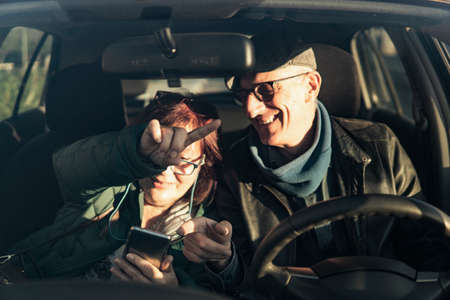 Retired couple on vacation consults directions on smart phone gps - active seniors traveling enjoy free time and retirement - focus on man handの写真素材