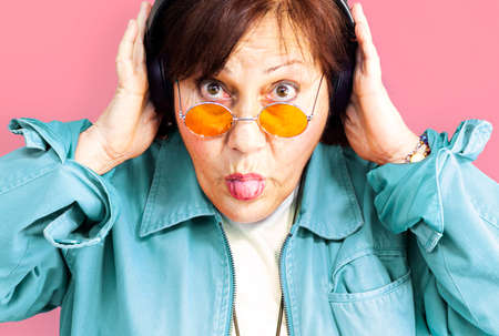 Portrait of middle aged woman listening to music with headphones - Close up of an older lady with...