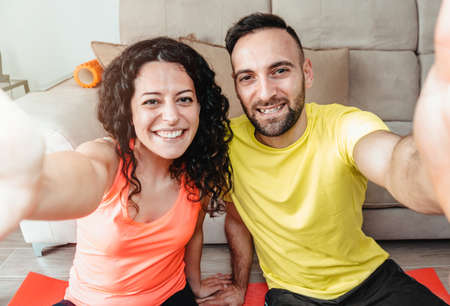 Engaged couple practice sports at home and take a selfie with their smartphone - lovers train...