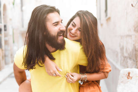 Happy couple on vacation have fun hugging each other - Young woman piggybacking on boyfriend playing and having fun outside - together lifestyle conceptの写真素材