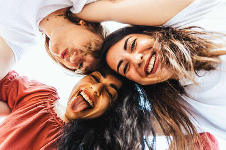 Best friends take a selfie from below with smartphone on vacation - group of happy multiracial tourists taking a funny photo - friendship and fun conceptの写真素材