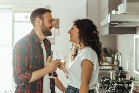 Young couple drinks a glass of white wine in the kitchen - couple in love celebrating their anniversary enjoying their new home - warm flare on backgroundの写真素材