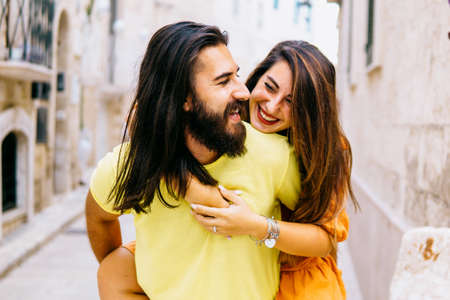 Happy couple on vacation have fun hugging each other - Young woman piggybacking on boyfriend playing and having fun outside - together lifestyle conceptの写真素材
