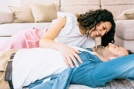 Portrait of a young couple in love hugging while lying on the carpet of their new home - millennial people relax in the living roomの写真素材