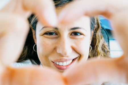 Woman smiles making heart gesture with handsの写真素材