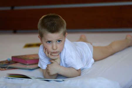 Child with book lying down on a bedの写真素材
