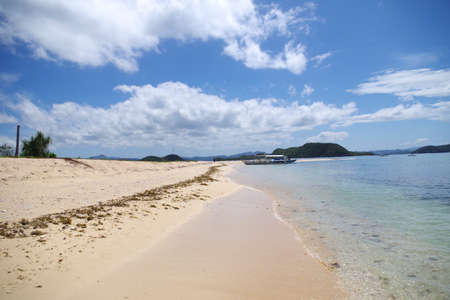 A palawan boat parked near a small island of the Philippines archipelago. The isle has a sandy beach and few growing palm trees. It's a beautiful sunny summer day, scattered clouds in the sky.の写真素材