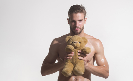Portrait of young man holding teddy bear. Young naked man with teddy bear. Young boy with teddy bear in hands. Happy man, brutal caucasian hipster, bearded macho with muscular torso holds plush toy.の写真素材