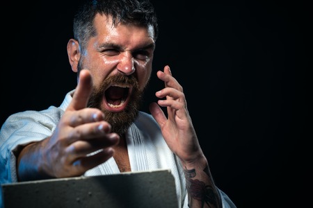 Karate man breaking with hand concrete brick. Sportsman martial art taekwondo training, in karate position. Brutal bearded man dressed in kimono practicing aikido.の写真素材