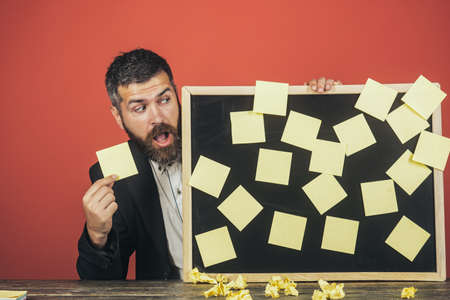 Business, planning, management, reminder and people concept - surprised handsome businessman holding black board with stickers. Bearded man in suit sticking adhesive notes on board.の写真素材