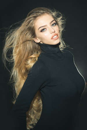 Haircare and health concept. Gorgeous long hair. Professional makeup. Romantic woman with long flying hair. Fashion woman hair style, model with long blonde waving hair wearing in black golf.の写真素材