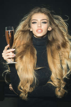Gorgeous romantic woman in stylish sweater, long hair waving on wind holds glass of champagne or...