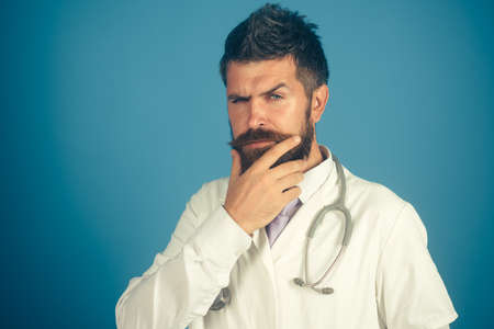 Concept of prevention, treatment and healthcare - confident serious male doctor with stethoscope. Serious bearded intern, physician, doctor in uniform holds his hand on his beard. Copy space.の写真素材