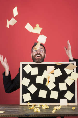 Bearded handsome male businessman sitting at table holds board on which pasted stickers. Joyful businessman in suit throws up stickers. Business, people, employment, career and hiring concept.の写真素材