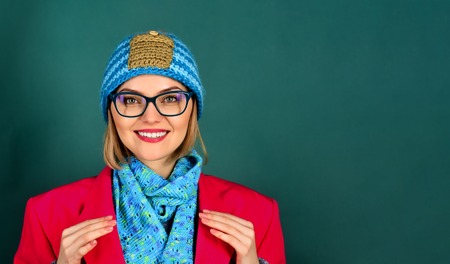 Autumn/winter fashion. Fashion woman wearing red jacket, hat, scarf in black glasses. Smiling girl in glasses with makeup, bright red lips, wears red coat, blue hat and scarf. Copy space for advertiseの写真素材