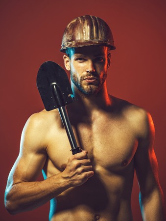 Builder or miner wears protective helmet holds shovel. Labour, industry man, repairman. Construction male worker portrait holds sapper shovel. Sexy builder, engineer in protective helmet with spade.の写真素材