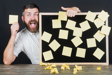 Bearded handsome male businessman sitting at table holds board on which pasted stickers. Notes,...