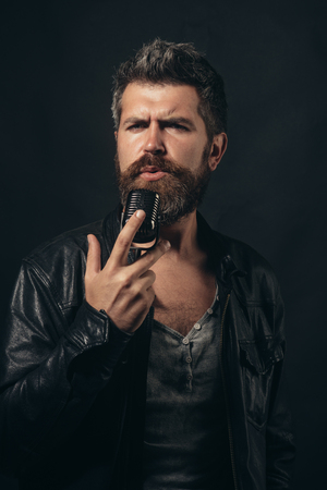 Singer, music, show business, people, technology, voice concept - bearded singer in elegant black jacket with microphone on stage. Super rock star, vocalist in dark. Male Rock Star singing at concert.の写真素材