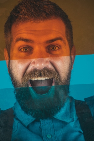 Positive face expression bearded man behind colored glass. Attractive macho with beard and moustache dressed in denim shirt. Color concept - vivid colors.の写真素材