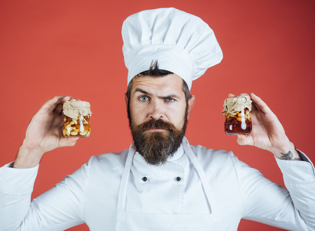 Portrait of serious bearded chef holding jar with honey nuts. Chef holding jar of layered nuts mix with honey topping. Healthy breakfast. Nutrition concept.の写真素材