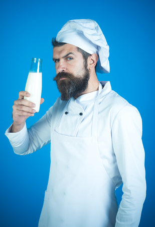 Chef with serious face in white apron and hat holds glass bottle fresh milk. Healthy soy milk, nutritious and delicious milk substitute. Restaurant dairy meal concept. Concept of cooking food.の写真素材