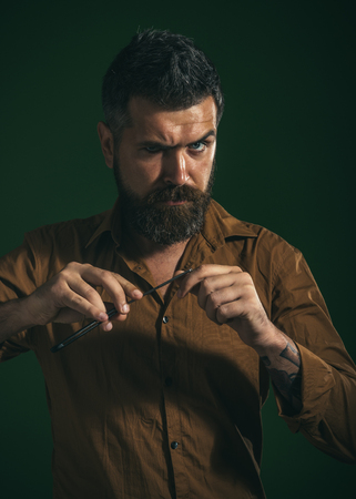 Professional barber. Barber equipment. Silhouette bearded man, macho with beard and moustache, holds in hands straight razor. Hairdresser in stylish shirt demonstrating sharp blade of dangerous razor.の写真素材