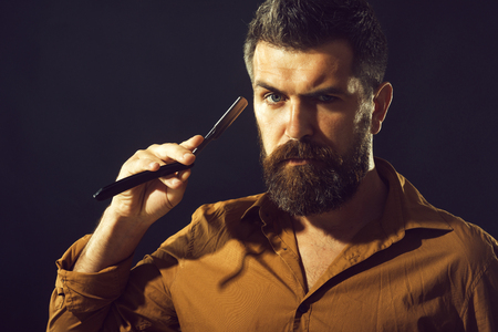 Tools for barber or shave. Attractive barber with black beard and mustache holds straight razor near his face. Bearded handsome sexy macho with straight razor. Unshaven man ready to shaving his beard.の写真素材