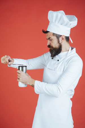 Cook man, serious chef in white uniform holding manual coffee grinder. Service, cafe, equipment, coffee concept - professional male cook, chef, barista grinds coffee with mechanical grinder in kitchenの写真素材