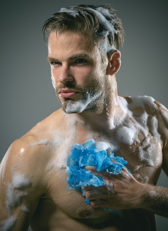 Macho washing with sponge. Man with beard is washed, sponge for body. Mucular attractive young man taking shower.の写真素材