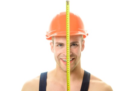 Happy builder, industrial worker, mechanic in construction helmet holds construction ruler near face. Macho with construction roulette. Sexy builder, engineer in construction helmet with tape measure.の写真素材