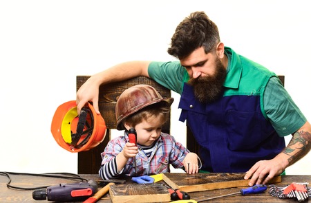Father teaches son repair case. Son and father repairing together. Bearded man with little assistante. Boy works with screwdriver. Repair and engineering education. Dad teaches little son to use toolsの写真素材
