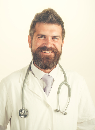 Medical, medicine, treatment, healthcare and ambulance services concept - cheerful bearded male physician with stethoscope in white uniform. Smiling doctor with beard, mustache in white medical gown.の写真素材