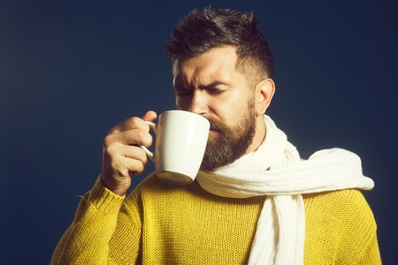 Handsome young man enjoying coffee or tea. Bearded young man holding cup with hot drink in hand - drinks and leisure concept. Hot drinks for cold time.の写真素材
