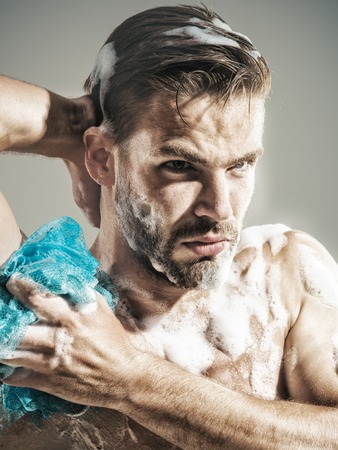 Healthy muscular sexy athlete taking shower, with soap sponge in hand. Handsome man, muscular sexy athlete, unshaven macho washing body with shower gel in bathroom.の写真素材