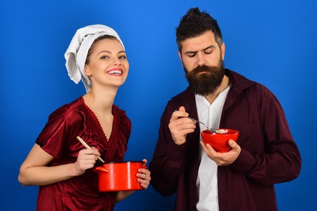 Couple prepares breakfast. People, love, feelings, relationship, food, lifestyle - loving couple man and woman. Sad bearded man holds red bowl, joyful girl holds pan. Human emotions, face expressions.の写真素材