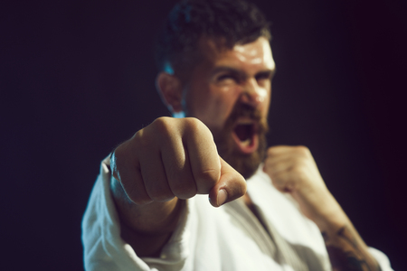 Strong arms and clenched fists. Portrait of screaming karate master instructor. Selective focus on fist. Brutal bearded man dressed in kimono practicing aikido.の写真素材