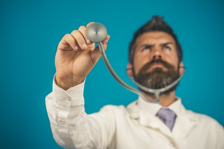 Healthcare, healthy lifestyle and medicine concept - medical bearded doctor with stethoscope in hand, focus on stethoscope. Diagnostic instrumen, hospital equipment. Advertising hospital, clinic.の写真素材