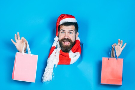 Christmas winter holidays celebration. Bearded man in santa hat and scarf through hole in blue...